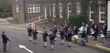 Pipers outside the old Schools building. A pipe band standing outside a large building.