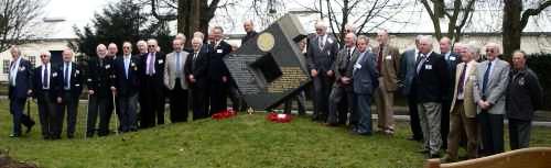 A group of men stood in a long line with a piece of squared sculpture in  the centre.